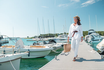 young pretty woman in white summer clothing walking by yachts dock