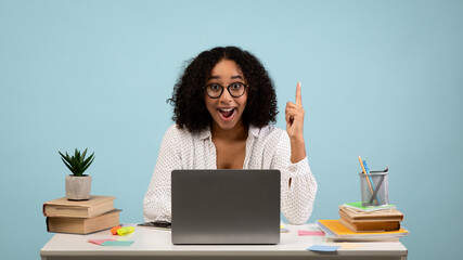 Millennial black female office worker having creative idea, gesturing eureka at workplace on blue studio background
