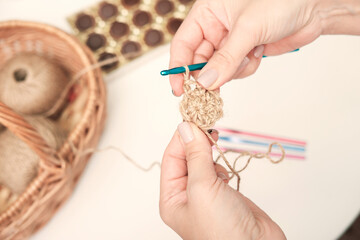 hands of a woman holding crochet and jute thread and fragment of a knitted pattern. natural eco knitting, hand made cup coaster. craft and hobby. Eco home decor