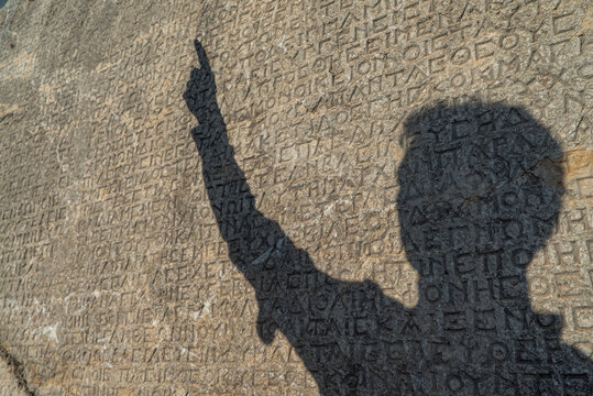 The man whose shadow falls on the ancient inscriptions written on the stone and his finger points to the writing