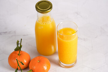 Tall glass with orange mango smoothie, several tangerines on white surface