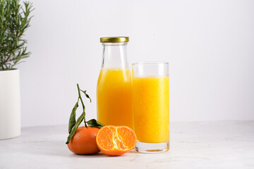 Tall glass with orange mango smoothie, several tangerines on white surface