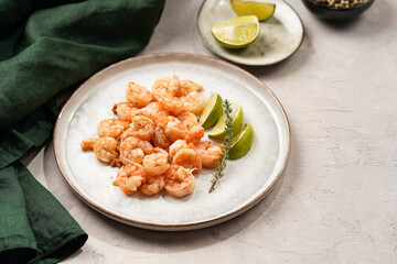 Grilled shrimps or tiger prawns served with lime, garlic and fresh herbs on scandi round plate on concrete surface. Pescatarian protein nutrition