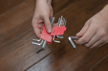 Hands hold a set of hex keys against the brown wooden floor. A g