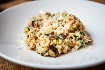 Delicious Italian vegetarian risotto cooked with mushrooms and onions served in white plate.