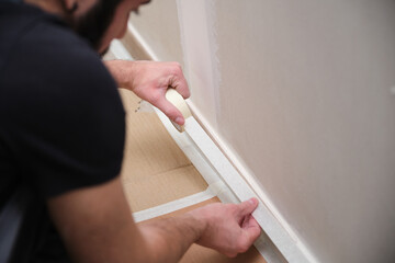 Unrecognizable painter using tape to cover the skirting board before painting.