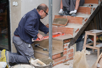 Senior bricklayer using a spirit level to check the step is horizontal.