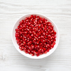 Red Pomegranate Seeds in a Bowl on a white wooden surface, top view. Flat lay, overhead, from above.
