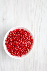 Red Pomegranate Seeds in a Bowl on a white wooden table, top view. Flat lay, overhead, from above. Space for text.
