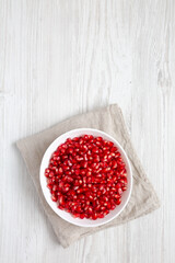 Red Pomegranate Seeds in a Bowl on a white wooden surface, top view. Flat lay, overhead, from above. Copy space.