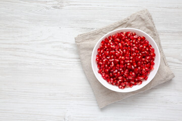 Red Pomegranate Seeds in a Bowl on a white wooden background, top view. Flat lay, overhead, from above.