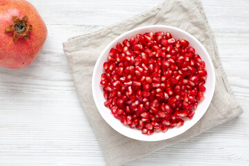 Red Pomegranate Seeds in a Bowl on a white wooden background, top view. Flat lay, overhead, from above.