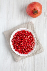 Red Pomegranate Seeds in a Bowl on a white wooden background, top view. Flat lay, overhead, from above.