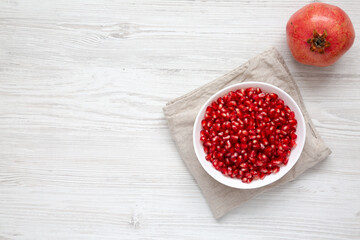 Red Pomegranate Seeds in a Bowl on a white wooden background, top view. Flat lay, overhead, from above. Copy space.