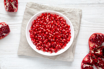 Red Pomegranate Seeds in a Bowl on a white wooden background, top view. Flat lay, overhead, from above.