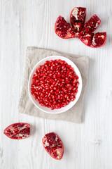 Red Pomegranate Seeds in a Bowl on a white wooden background, top view. Flat lay, overhead, from above.