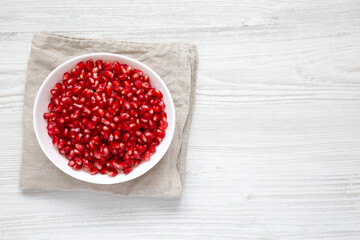 Red Pomegranate Seeds in a Bowl on a white wooden background, top view. Flat lay, overhead, from above. Space for text.