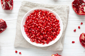 Red Pomegranate Seeds in a Bowl on a white wooden table, top view. Flat lay, overhead, from above.