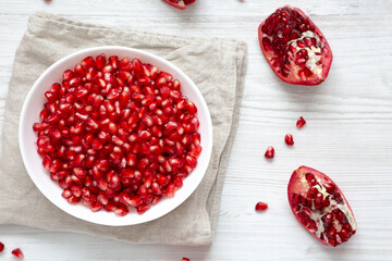 Red Pomegranate Seeds in a Bowl on a white wooden surface, top view. Flat lay, overhead, from above.