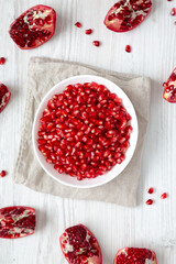 Red Pomegranate Seeds in a Bowl on a white wooden surface, top view. Flat lay, overhead, from above.