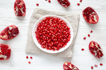 Red Pomegranate Seeds in a Bowl on a white wooden surface, top view. Flat lay, overhead, from above.