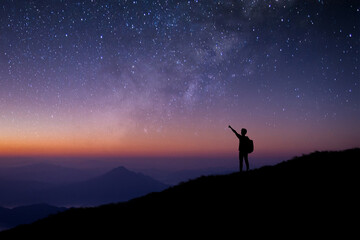 Silhouette of young man standing and open arms watched the star, milky way and night sky alone on top of the mountain. He enjoyed traveling and was successful when he reached the summit.