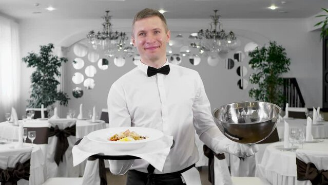 Male waiter opens the lid of a tray with a hot dish