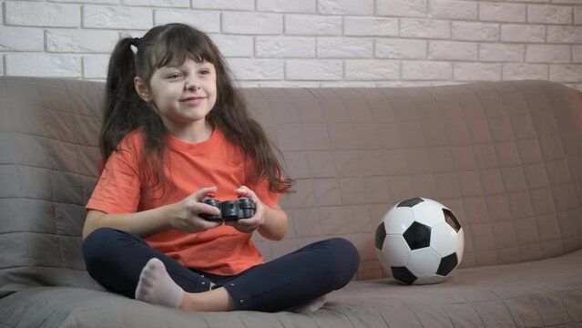 Football on play station. A little fan has a leisure with a console in the room. A cute little girl is playing with a prefix.
