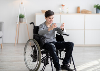 Positive disabled teenager in wheelchair having video call on smartphone at home