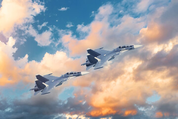 A pair of tandem military fighter jets fly in the sky against the backdrop of beautiful clouds at...
