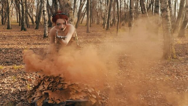 Terrible queen of autumn. Halloween party. Gorgeous witch in an autumn dress with a smoke bomb. Beautiful she-devil beckons.Horror concept.
