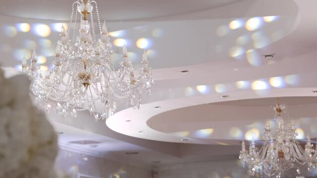 White multi-level plasterboard ceiling with rich crystal chandeliers in the hall, close-up. Ceiling is decorated with white festive circles of light.
