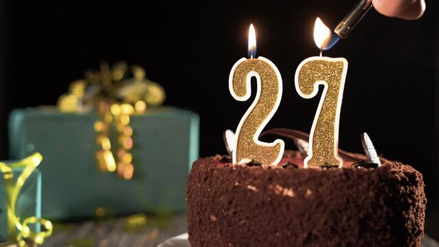 Birthday cake with candles number 27 on a bright festive background, fire from a lighter, blow out twenty-seven years.