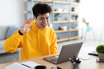 Smiling asian man working on laptop waving hand