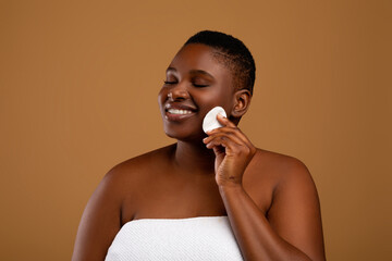 Portrait of curvy black woman cleaning skin by cotton pad