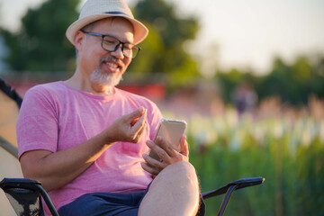 Middle-aged man visits online dating site via sat on phone in flower garden, focus on hand
