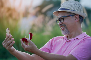 Surprised.Online video call, Happy Asian grey beard man with eyeglasses marriage proposal to girlfriend online on Laptop computer. Diamond ring in red box. New normal valentine Quarantine concept..