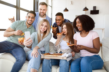 Happy diverse friends having party, sitting on sofa with pizza, chips and cellphone, socializing at home