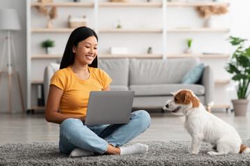 Cheerful asian woman using laptop, playing with dog