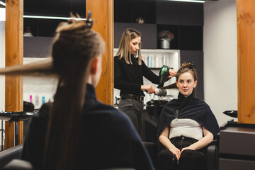 Master woman hairdresser dries the girl's hair with a hairdryer after washing in a beauty salon.