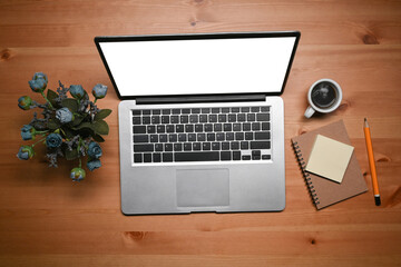 Above view laptop computer, coffee cup, notebook and flowers on wooden table.