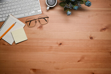 Above view keyboard, glasses, coffee cup and notebook on wooden table.