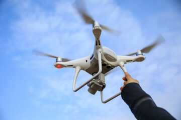 Fototapeta na wymiar Hand reaching a white drone with camera flying against blue sky