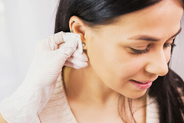 Side view photo of a beautiful brunette woman preparing to a piercing procedure and doctor in...