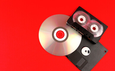 Audio cassette, floppy disk and disc on a red background. Legacy technologies