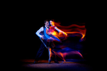 Dynamic portrait of young ballroom dancers dancing Argentine tango isolated on dark background with...