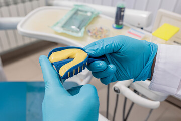 dentist wearing protective gloves squeezes out the mass into the articulator with teeth mould. - obrazy, fototapety, plakaty