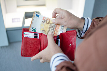 Unrecognizable female holding in hands wallet with euro money near the ATM. Withdrawing cash to pay...