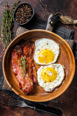 Traditional English breakfast with fried eggs and bacon in wooden plate. Dark background. Top view