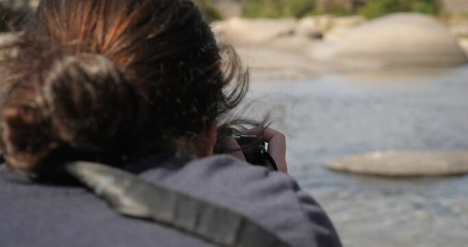 Shot from behind a woman taking pictures of the river in California during summer.